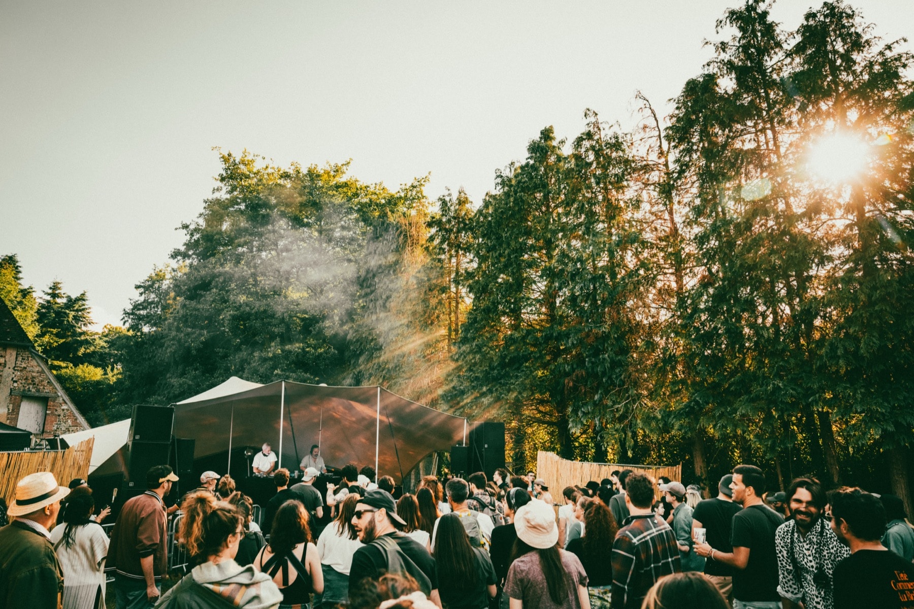 La scène du Biches Festival au soleil couchant, le public de dos entre les arbres.